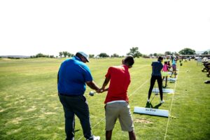 Instructor teaching golf at an outdoor course with students practicing their swings.