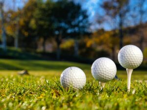 Three golf balls on tees ready for play on a bright sunny day in a green field.